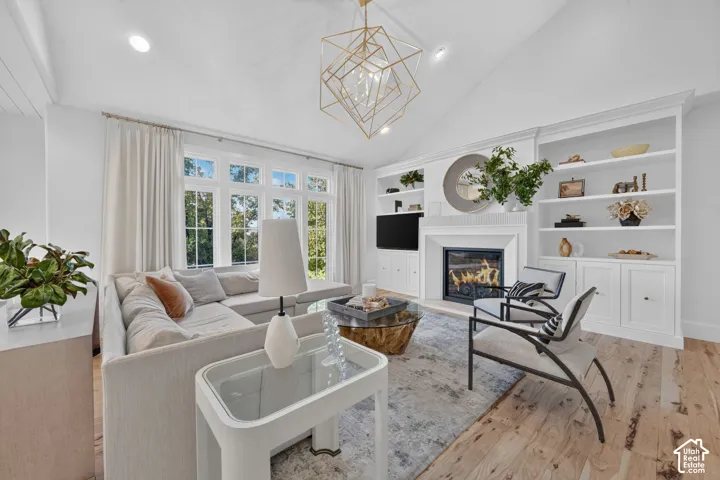 Vaulted ceiling with shiplap accents, large multi-pane windows, wood-finish flooring, built-in shelving, and a fireplace with a mantel
