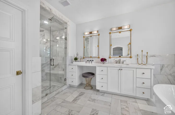 Glass-enclosed shower with a built-in bench, dual vanity with undermount sinks, white cabinetry, integrated dressing table, and patterned tile flooring