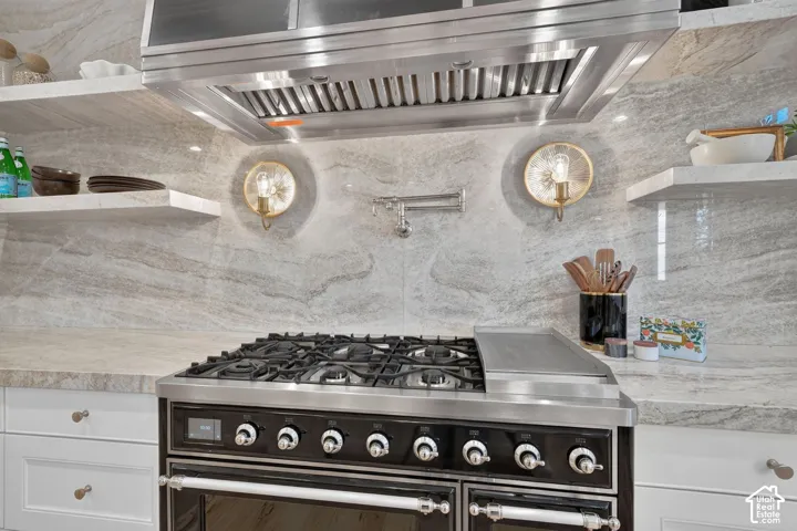 Chef's kitchen featuring a professional-grade dual-fuel range with eight burners and dual convection ovens, stainless steel range hood with baffle filters, polished stainless steel countertops, soft-close cabinetry, and elegant stone tile backsplash with