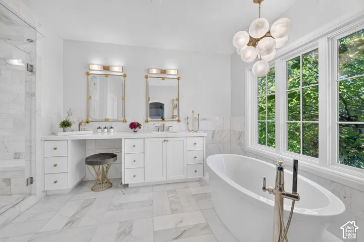 Freestanding soaking tub, dual vanity with built-in dressing area, glass-enclosed shower, mosaic tile flooring, and multiple windows