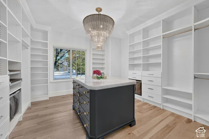 Expansive custom closet featuring extensive built-in shelving, hanging rods, wood-finish flooring, and a central island with a light-toned countertop