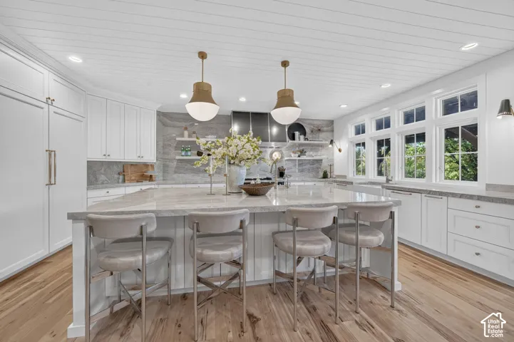 Expansive kitchen island with seating, white shaker cabinetry, light wood-finish flooring, recessed lighting, and a paneled ceiling