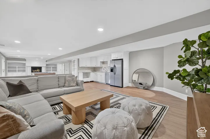 Open-concept living space with wood-finish flooring, recessed lighting, and a built-in wet bar featuring a stainless steel refrigerator