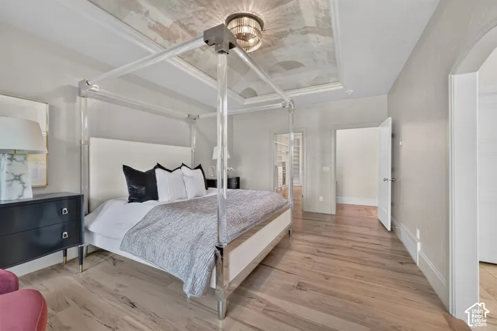 Light wood-finish flooring, tray ceiling with decorative finish, recessed lighting, and an arched doorway