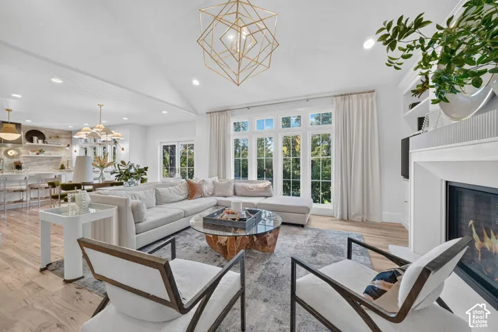 Vaulted ceiling with gold-tone geometric chandelier, light wood-finish flooring, built-in shelving, white framed windows, and a built-in fireplace