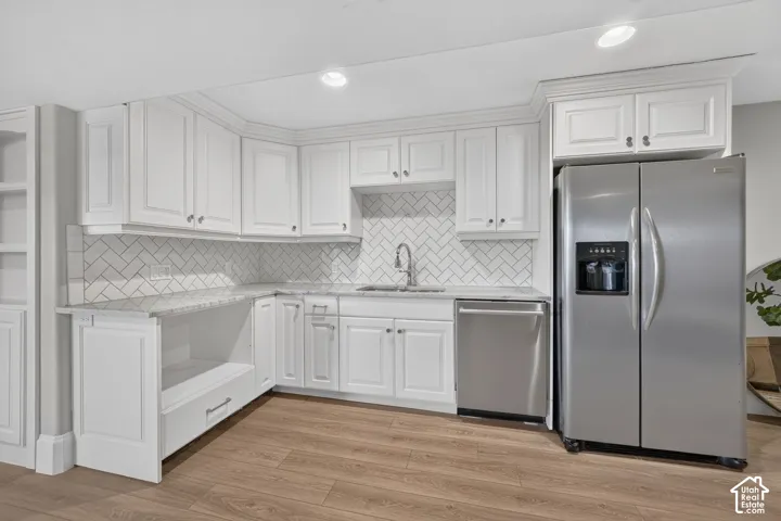 White shaker-style cabinetry, stainless steel appliances, herringbone tile backsplash, light wood-finish flooring, and recessed lighting