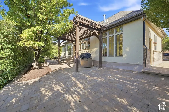 Expansive paver patio with a wood pergola, stucco exterior, and multi-pane windows
