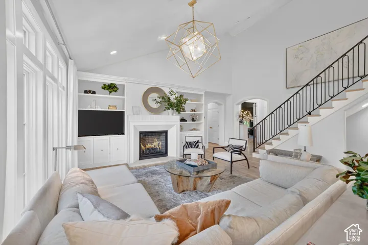 Vaulted ceiling living area featuring a fireplace with a white mantel, built-in shelving, large windows, and a staircase with a black wrought iron railing