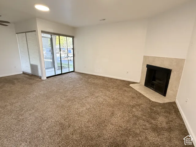 Living area featuring warm-toned carpeting, a corner fireplace with a tiled surround, and sliding glass doors