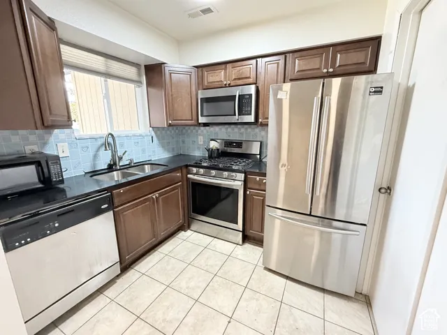 Kitchen featuring wood-finish cabinetry, black countertops, stainless steel appliances, and a tiled floor