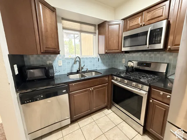 Kitchen featuring wood cabinetry, stainless steel appliances, dark countertops, a tile backsplash, and tile flooring