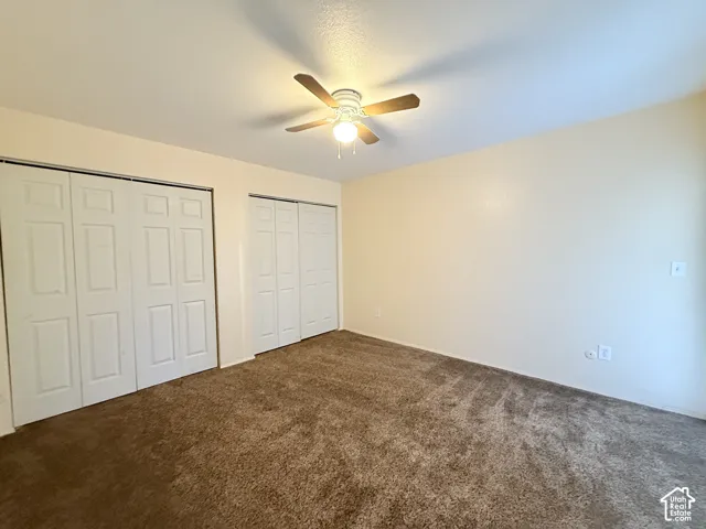 Plush carpeting, two bi-fold door closets, and a ceiling fan with integrated lighting