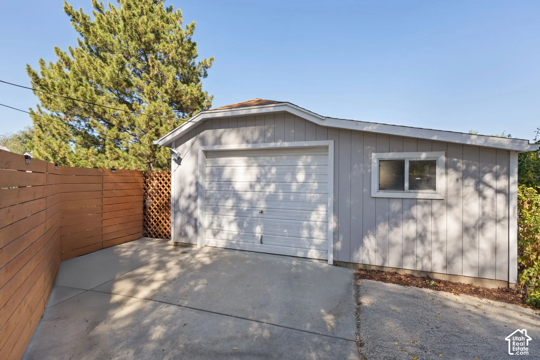 Detached garage with a single vehicle door and side window, concrete driveway, and wood privacy fencing