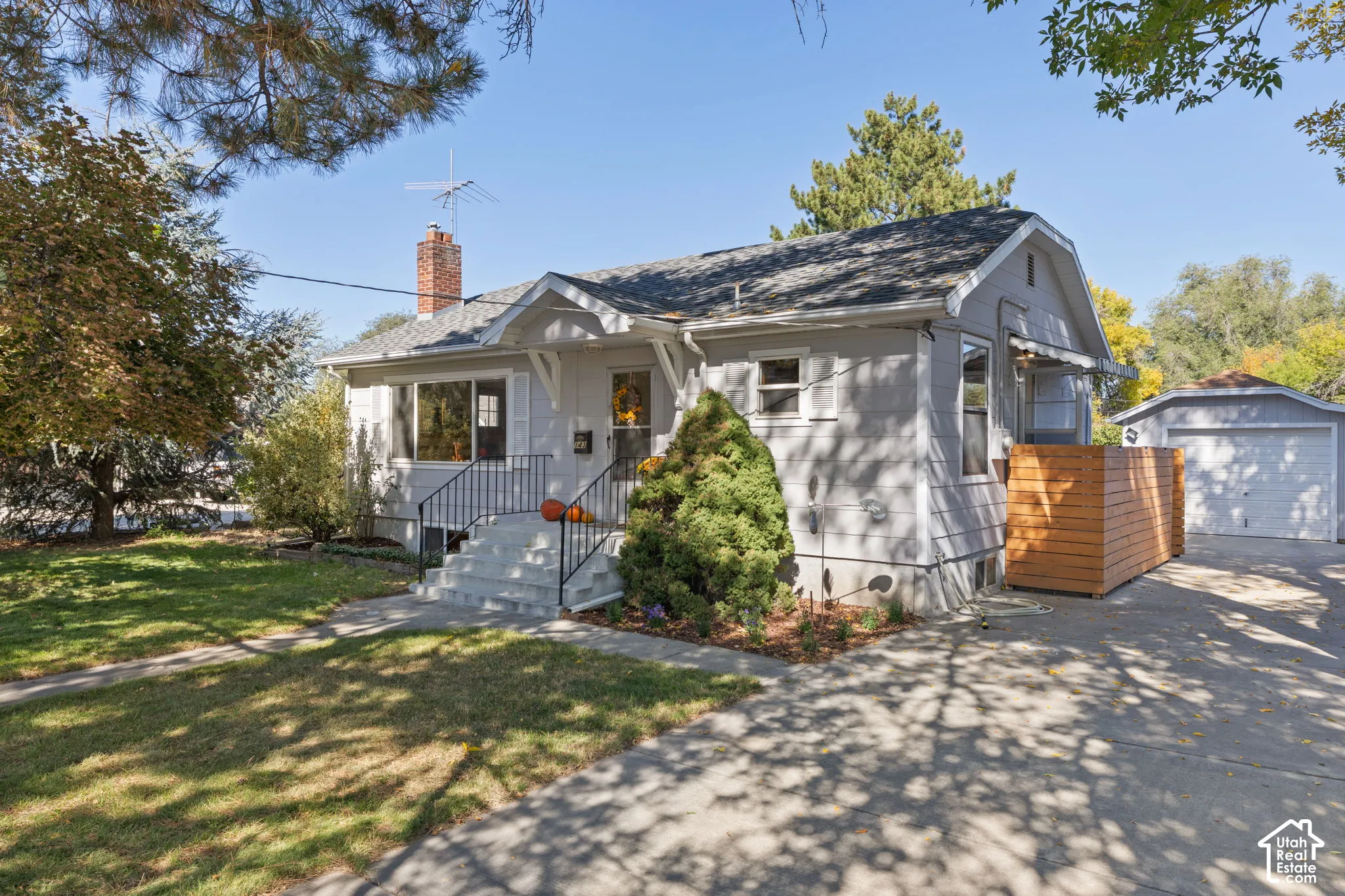 Light gray exterior with white trim, brick chimney, concrete steps with black railings, and a two-car garage