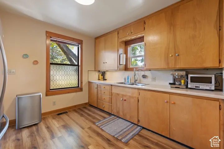 Wood-finish flooring, light wood cabinetry, light-toned countertops, and a stainless steel sink with a chrome faucet