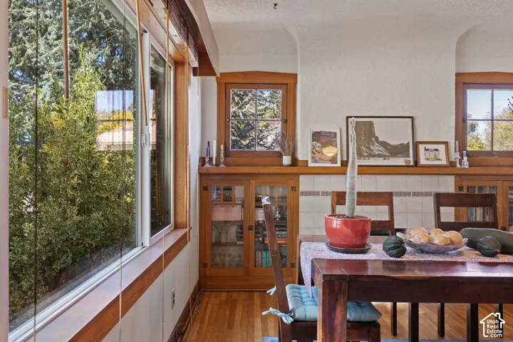 Wood-finish flooring, built-in wooden cabinetry with glass inserts, wood-trimmed windows, and a tiled accent wall