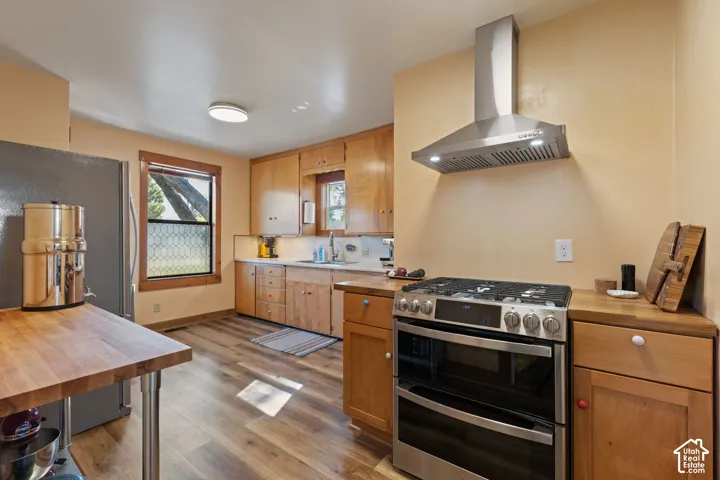 Natural wood-finish flooring, stainless steel range with double ovens, stainless steel range hood, natural wood cabinetry, and wood countertops