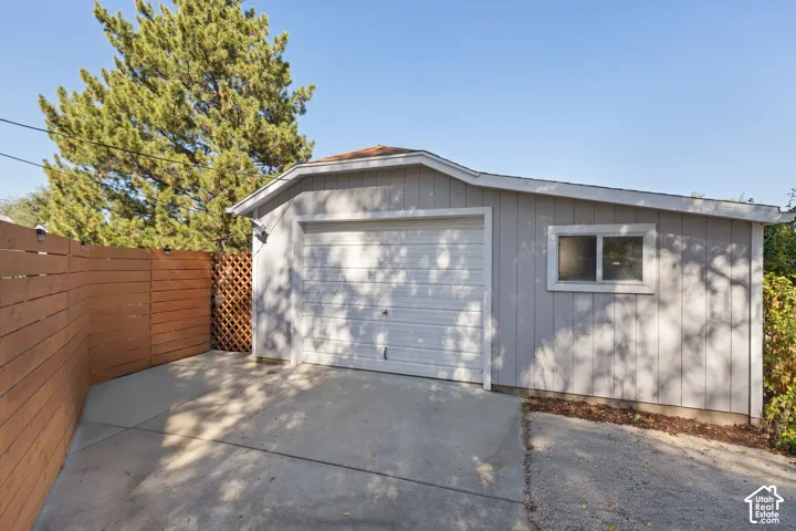 Detached garage with a single vehicle door and side window, concrete driveway, and wood privacy fencing