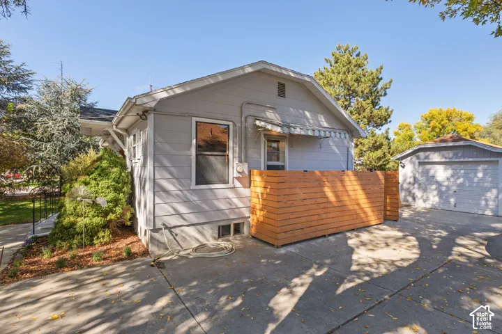 Detached garage with a paneled door, concrete driveway, horizontal wood panel fencing, and a white awning
