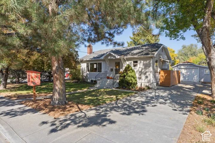 Single-story residence with a light-colored exterior, an asphalt driveway, mature trees, and a detached garage