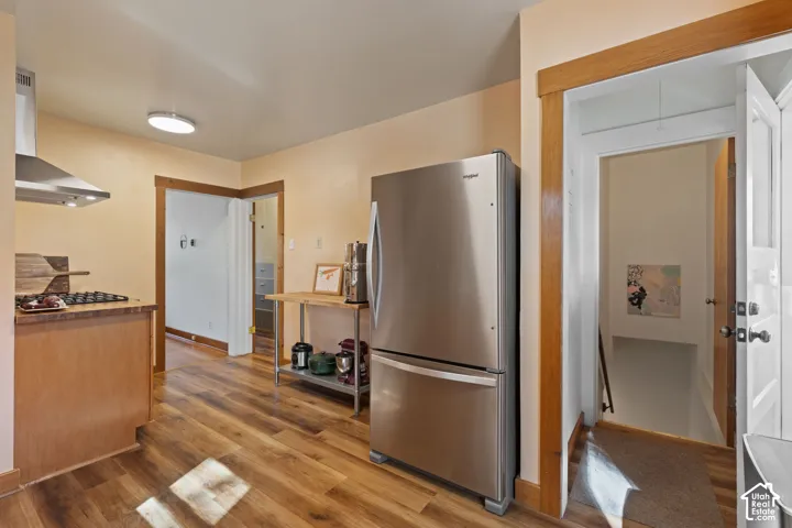 Wood-finish flooring throughout, stainless steel refrigerator, stainless steel range hood, and a built-in cooktop