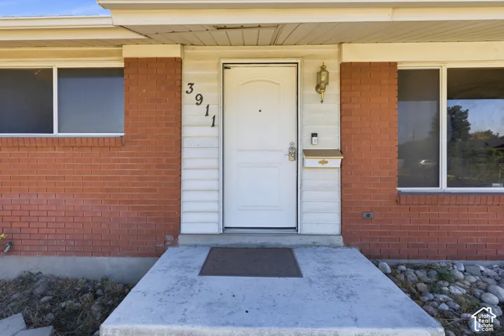 Red brick exterior with white siding accents, a white entry door, and an exterior wall lantern