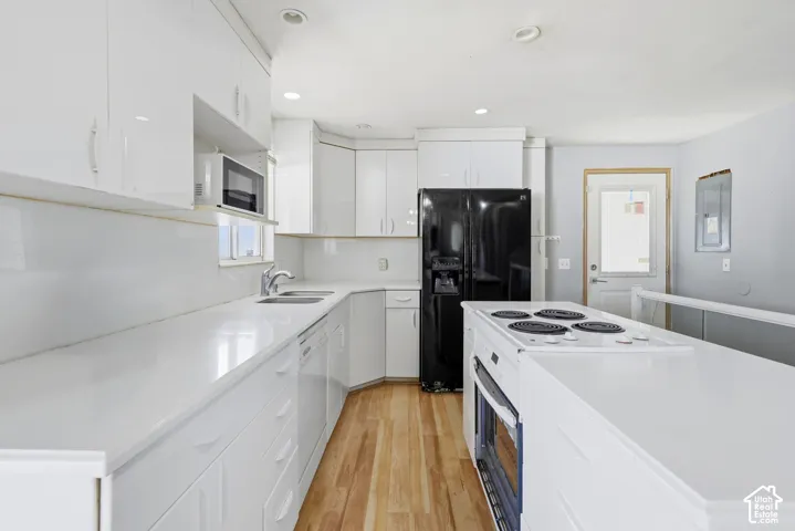 Kitchen featuring white cabinetry, white countertops, built-in microwave, stainless steel sink, and wood-finish flooring