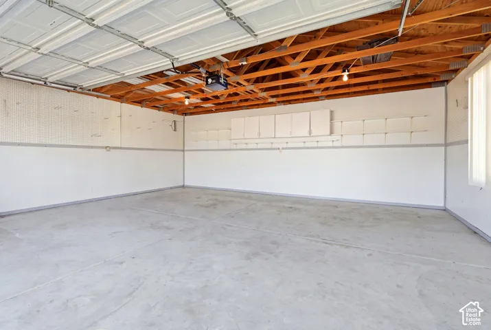 Spacious garage with exposed wood ceiling beams, concrete flooring, and built-in white cabinetry