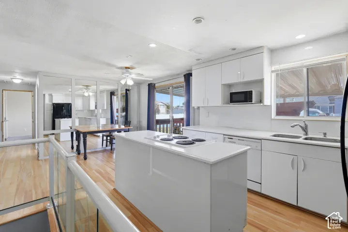 Kitchen featuring a central island with cooktop, white cabinetry, integrated sink, and wood-finish flooring