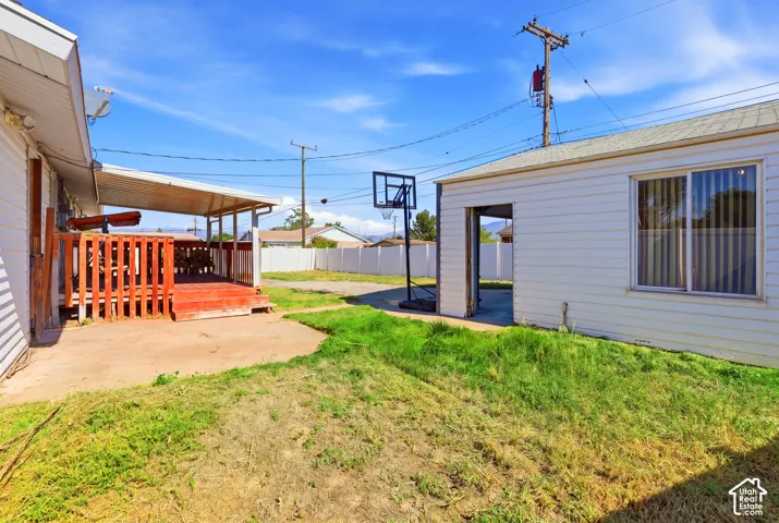 Covered deck with painted wood railing, adjacent concrete patio, and separate structure with a window