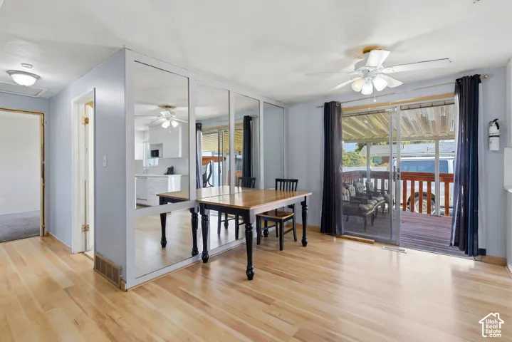 Wood-finish flooring throughout, mirrored wall feature, ceiling fan with integrated lighting, sliding glass door, and a covered deck