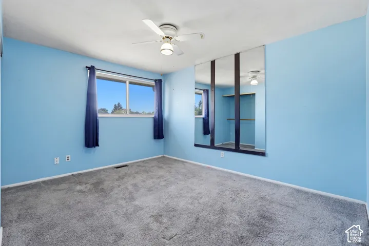 Ceiling fan with integrated lighting, large window, wall-to-wall carpeting, and a mirrored built-in closet