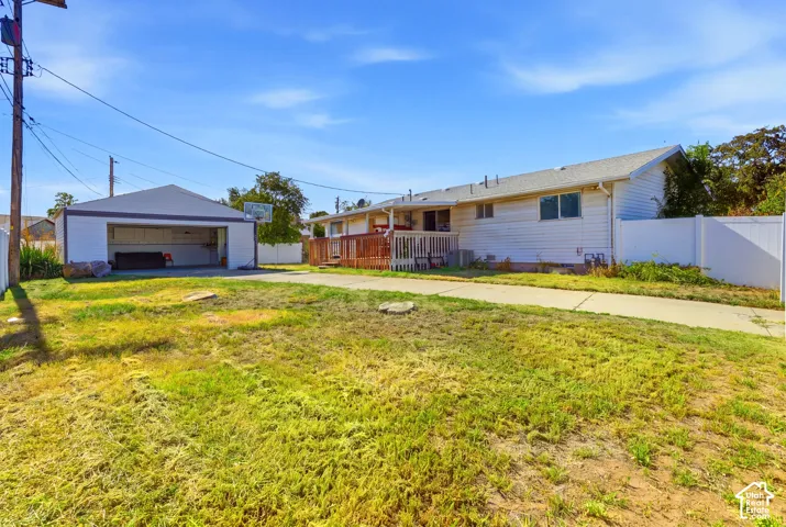 Detached garage with open bay, wood deck, white vinyl fencing, and concrete driveway