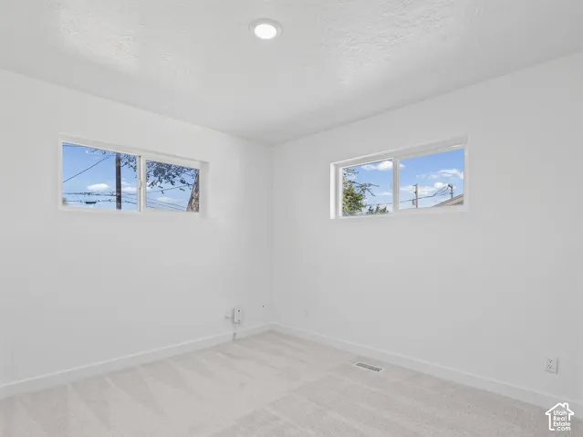 Recessed ceiling lighting illuminates the room with light-toned carpet flooring and two windows