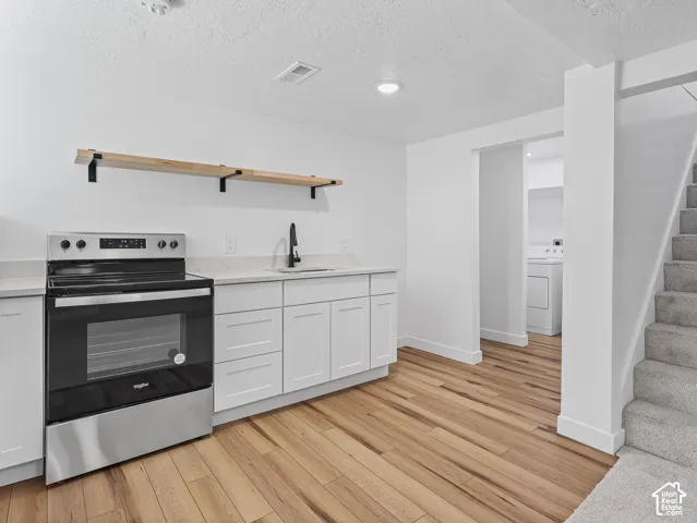 Stainless steel range, white cabinetry, open shelving, wood-finish flooring, and a carpeted staircase