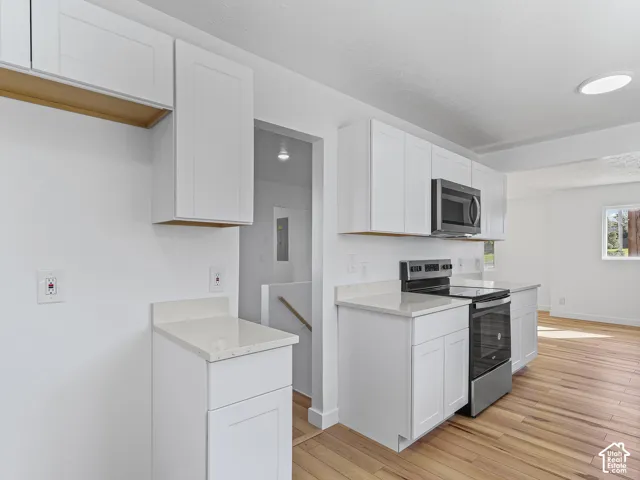 White shaker cabinetry, light-colored countertops, stainless steel appliances, wood-finish flooring, and a recessed ceiling light