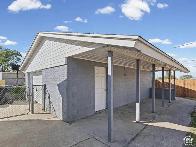 Covered carport with concrete flooring, brick exterior, garage access, and chain link fencing