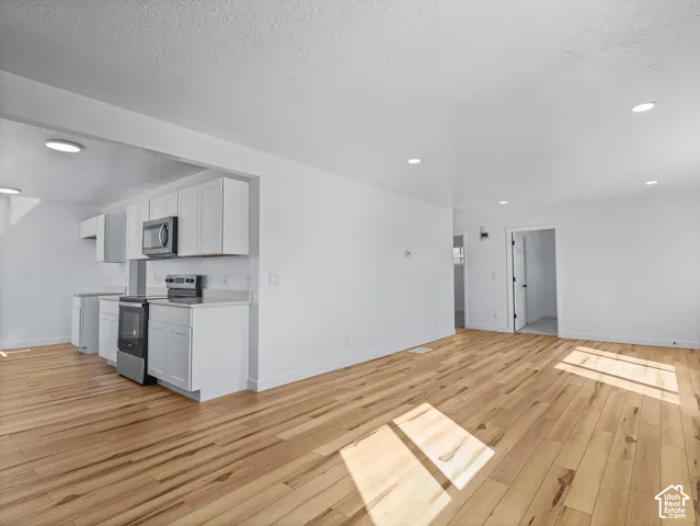 Open-concept living space featuring wood-finish flooring, recessed lighting, and a kitchen with white cabinetry and stainless steel appliances
