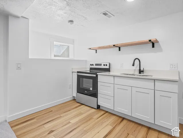Stainless steel range, wood-finish flooring, white cabinetry, integrated sink with matte black faucet, and open wood shelving