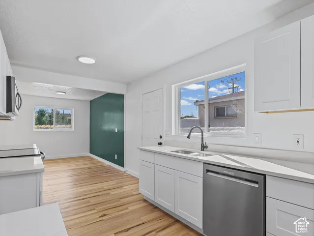 Kitchen featuring white shaker cabinetry, light-toned countertops, a stainless steel sink with a dark-finish faucet, and wood-finish flooring