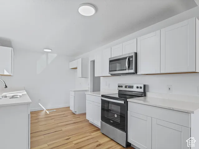 Kitchen featuring wood-finish flooring, white cabinetry, integrated stainless steel appliances, and solid surface countertops