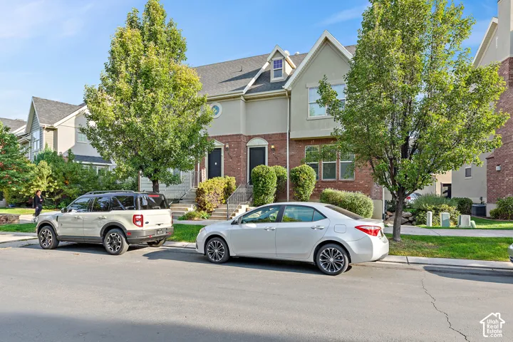 Two-story townhome with brick and stucco exterior, prominent gabled dormer, and mature landscaping