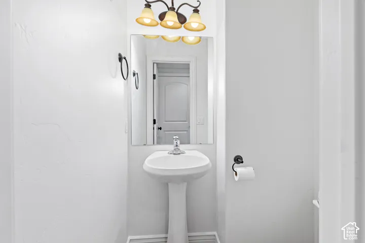 Pedestal sink with chrome faucet, wall-mounted mirror, and decorative light fixture