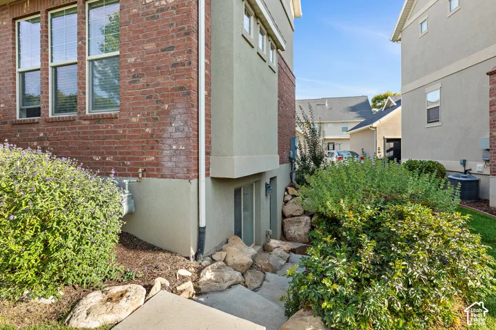 Brick and stucco exterior with multiple windows, concrete steps, and established landscaping