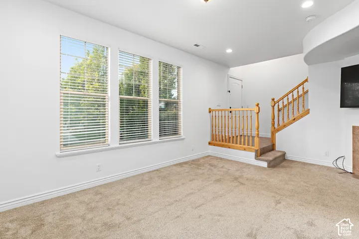 Triple windows with white blinds, neutral carpet flooring, recessed lighting, and a wooden staircase with baluster railing