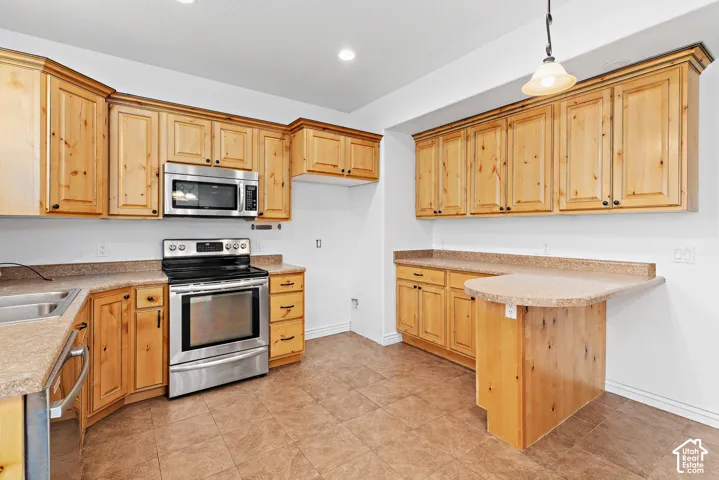Kitchen featuring wood cabinetry, stainless steel appliances, a corner sink, a peninsula with counter seating, and tile flooring