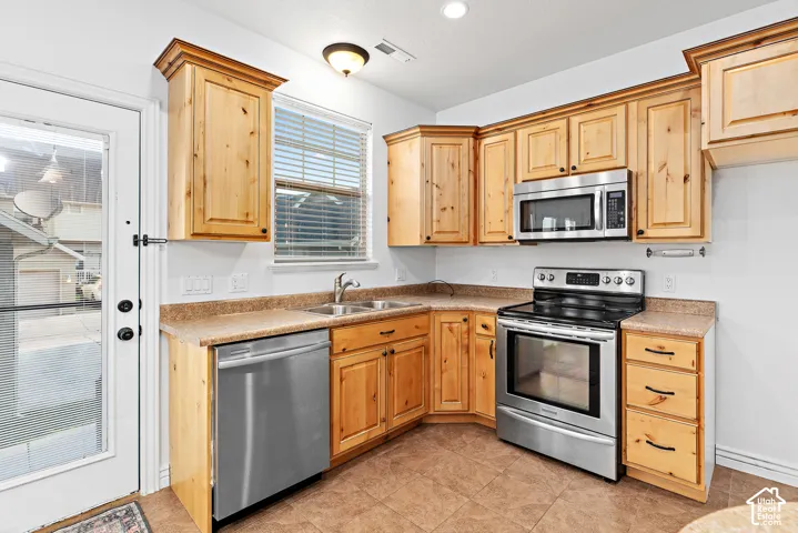 Kitchen featuring light wood cabinetry, stainless steel appliances, a double basin sink, and a glass-paneled exterior door