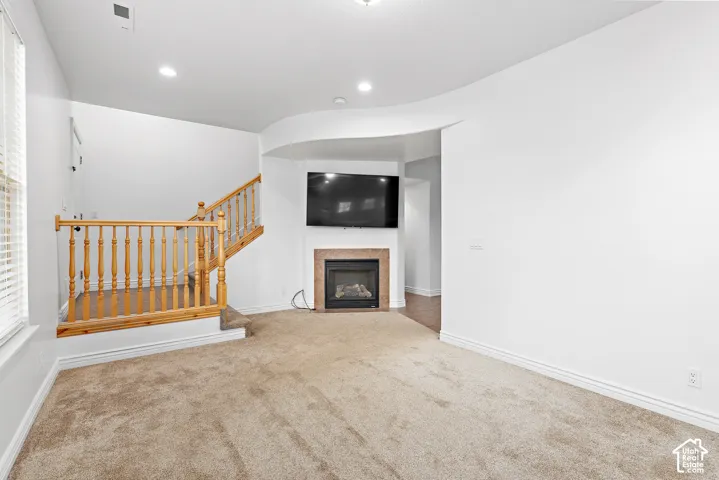 Built-in fireplace with a stone surround, recessed lighting, carpeted flooring, and a wood staircase
