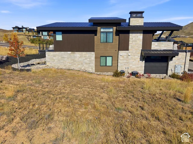 Modern exterior featuring a dark metal roof, stone facade, horizontal wood-finish siding, and a two-story design