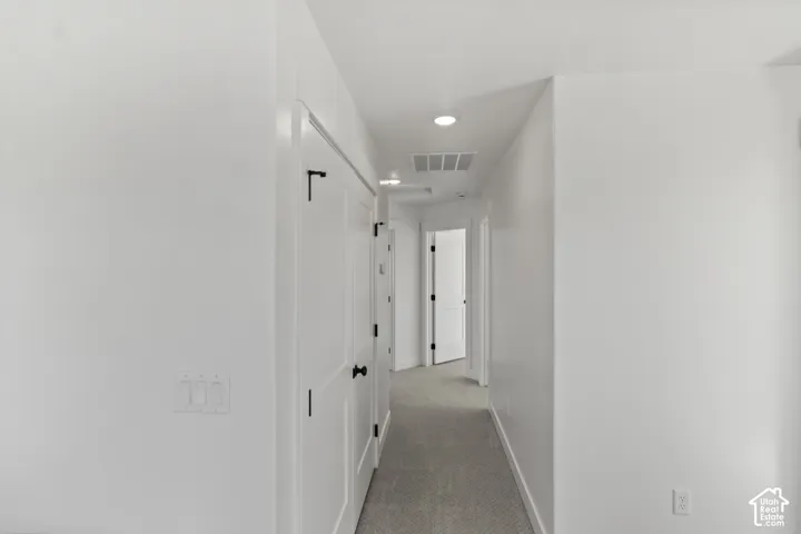 Hallway featuring white walls, white doors with dark hardware, recessed ceiling lighting, and carpet flooring